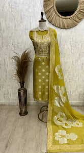Green and white traditional outfit with a floral dupatta on a mannequin against a textured wall.