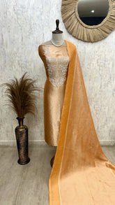 Mannequin wearing a beige dress with a matching dupatta against a textured wall.