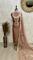 Brown traditional outfit with gold embroidery on a mannequin against a textured wall.