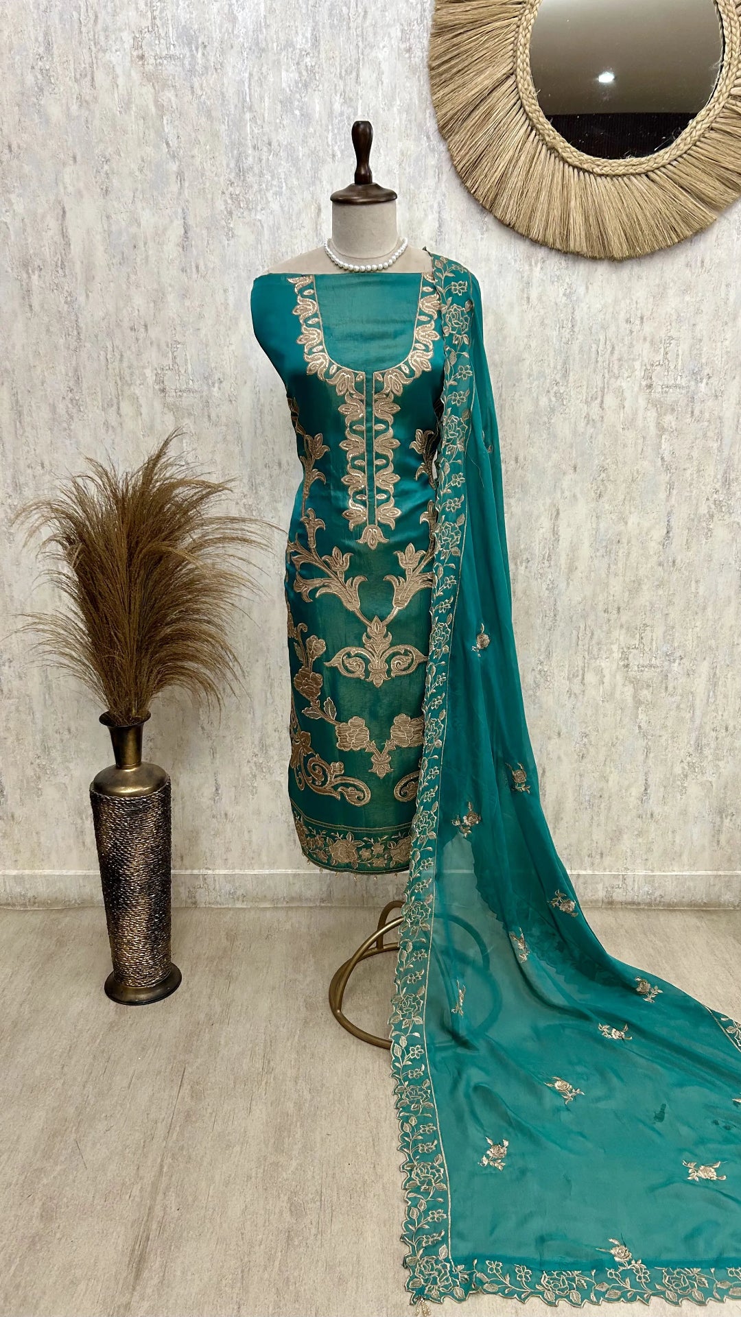 Teal embroidered dress with dupatta on a mannequin against a light gray wall.