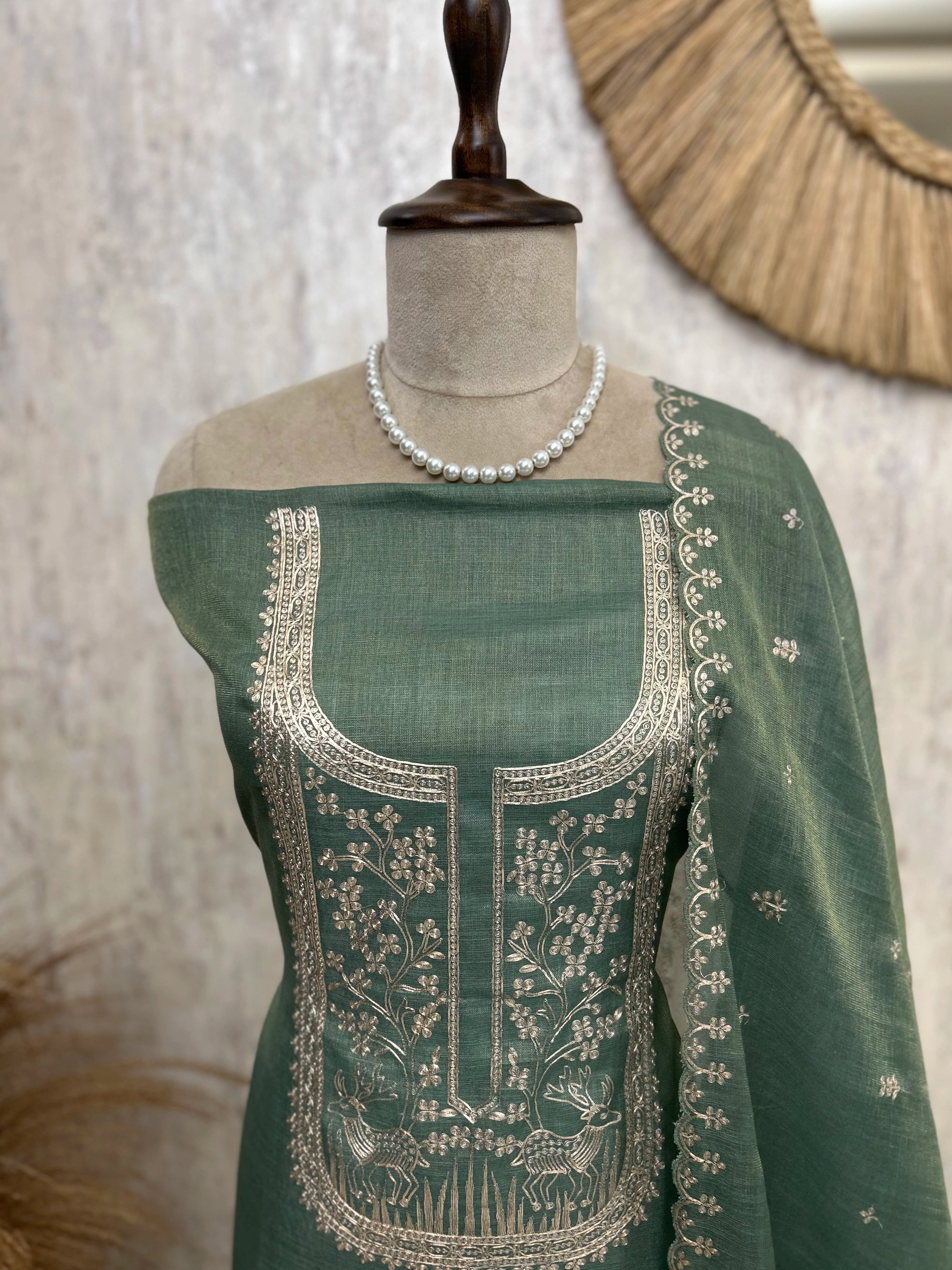 Green embroidered garment on a mannequin with a pearl necklace against a neutral background