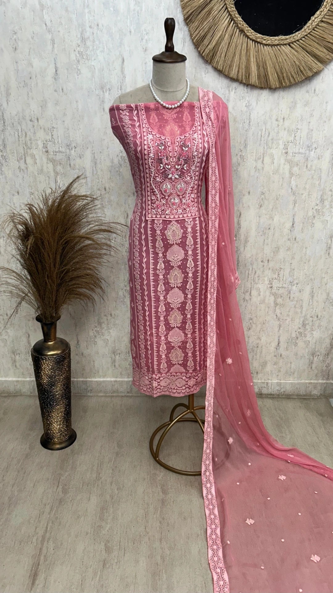 Pink embroidered dress with a dupatta on a mannequin against a textured wall.